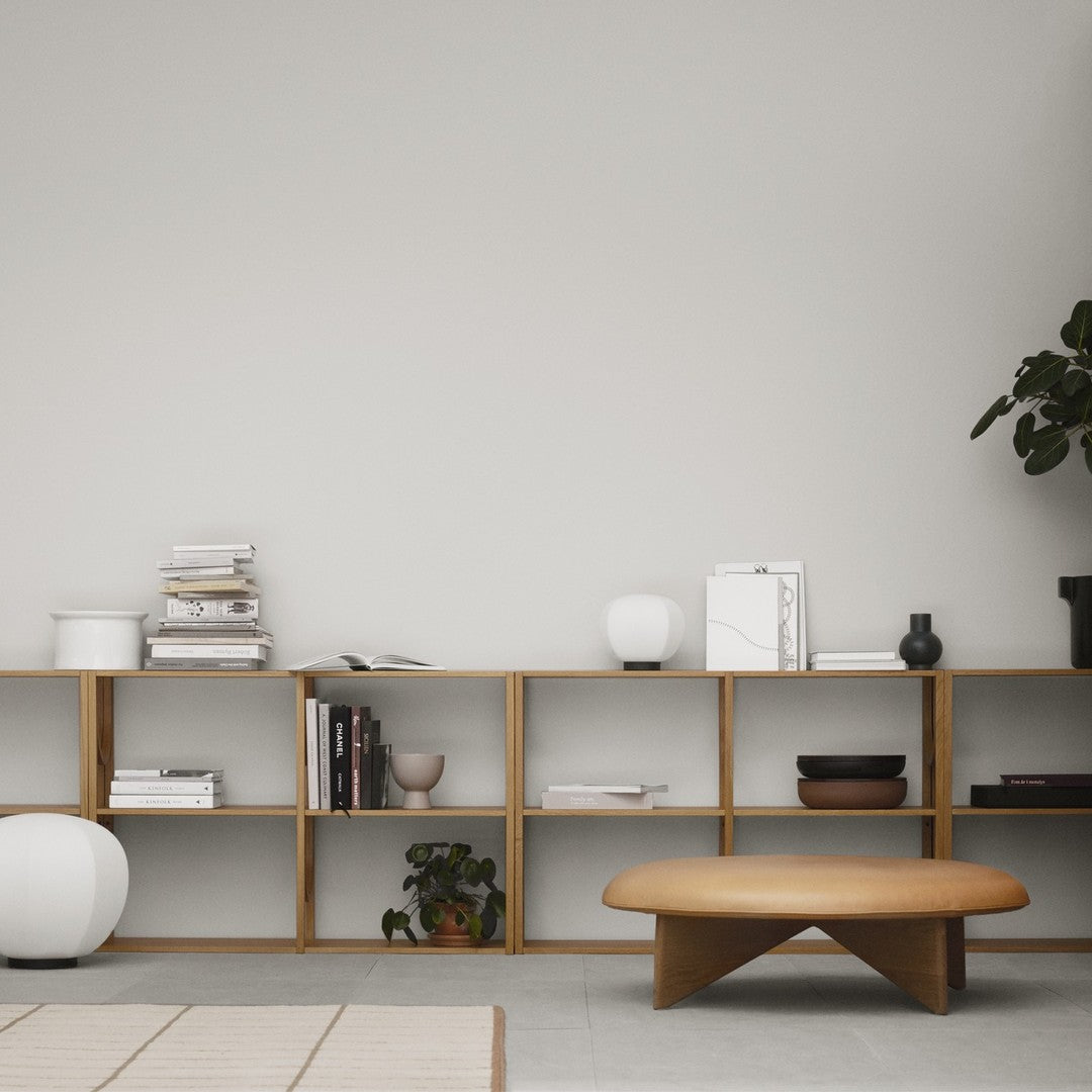 Wooden shelving unit with natural finish, white ceramics, and a round wooden coffee table on a neutral backdrop.