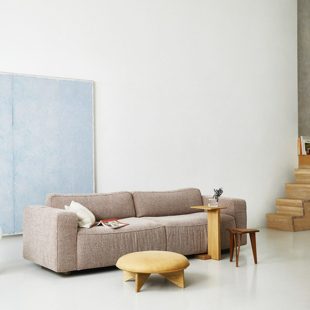 Cozy taupe sofa with textured fabric, paired with a round, yellow ottoman and natural wood accents, on a minimalist backdrop.