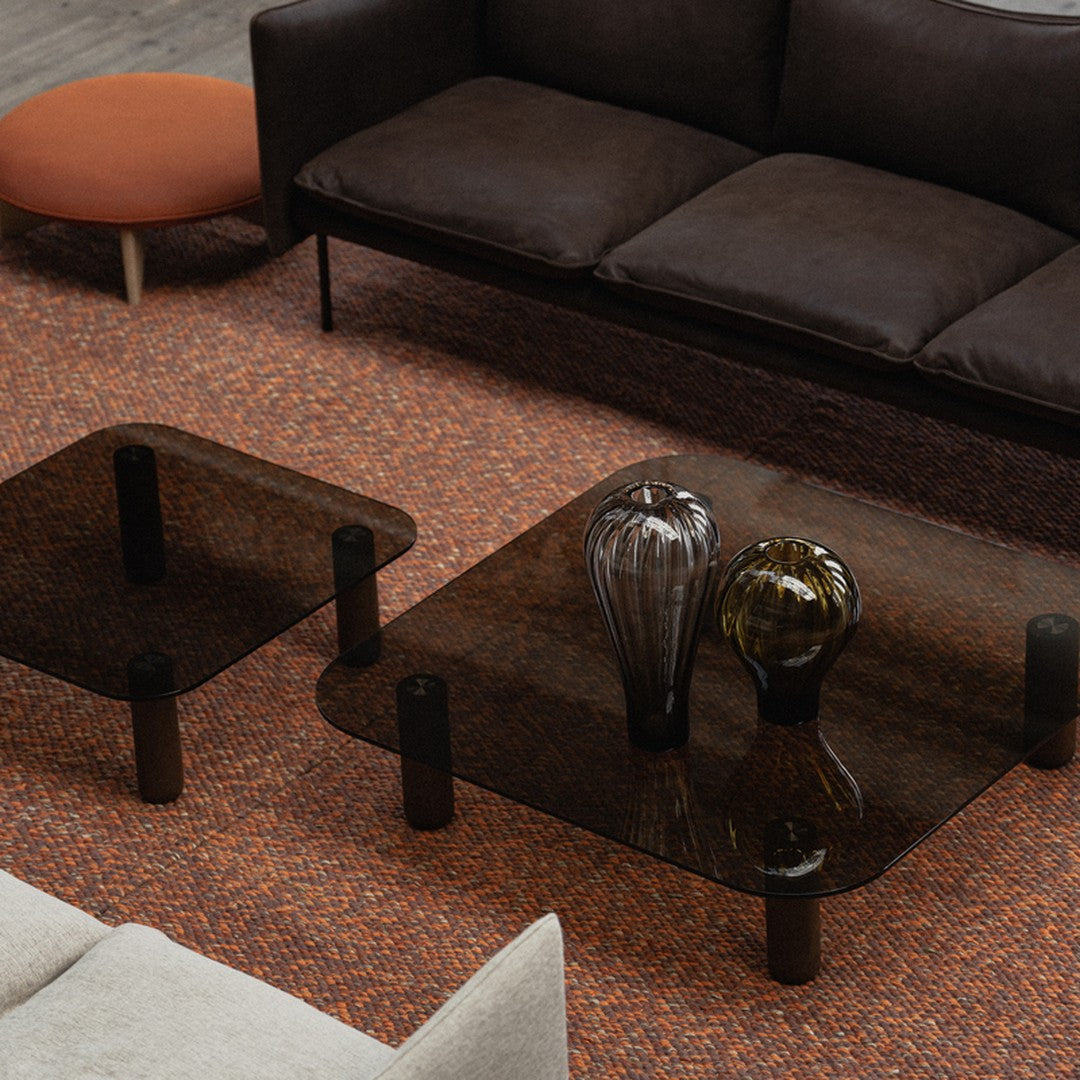 Brown and orange textured area rug with dark glass coffee tables and decorative vases on a modern living room setting.