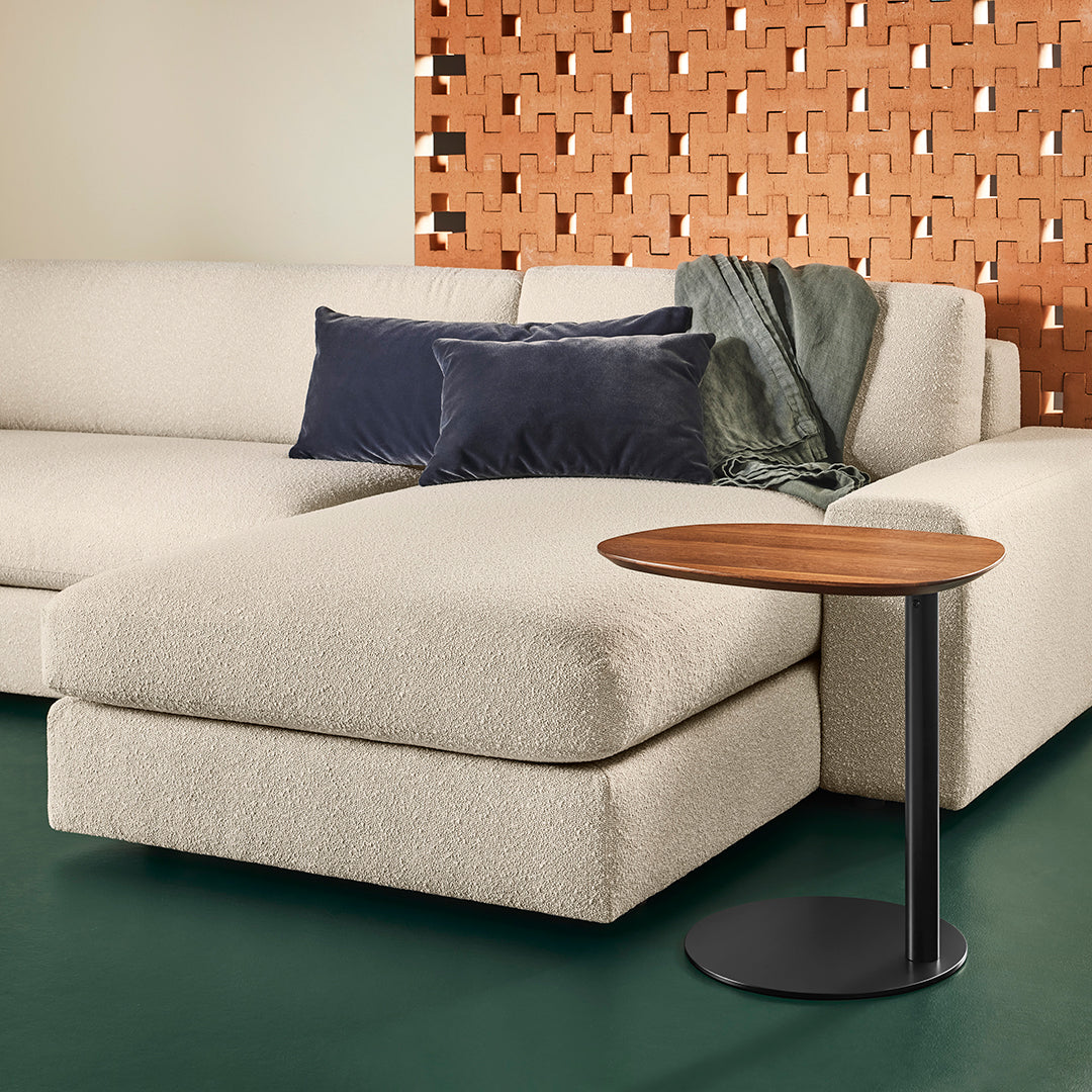 Beige sectional sofa with navy pillows, cozy green throw, and a round wooden side table on a dark green floor.