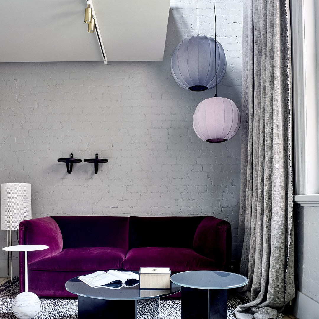 "Luxurious violet velvet sofa with soft gray walls, paired with purple and lavender hanging lamps and geometric black tables."