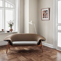 Brown and white curvy sofa with wooden legs, set against a neutral wall and parquet flooring.