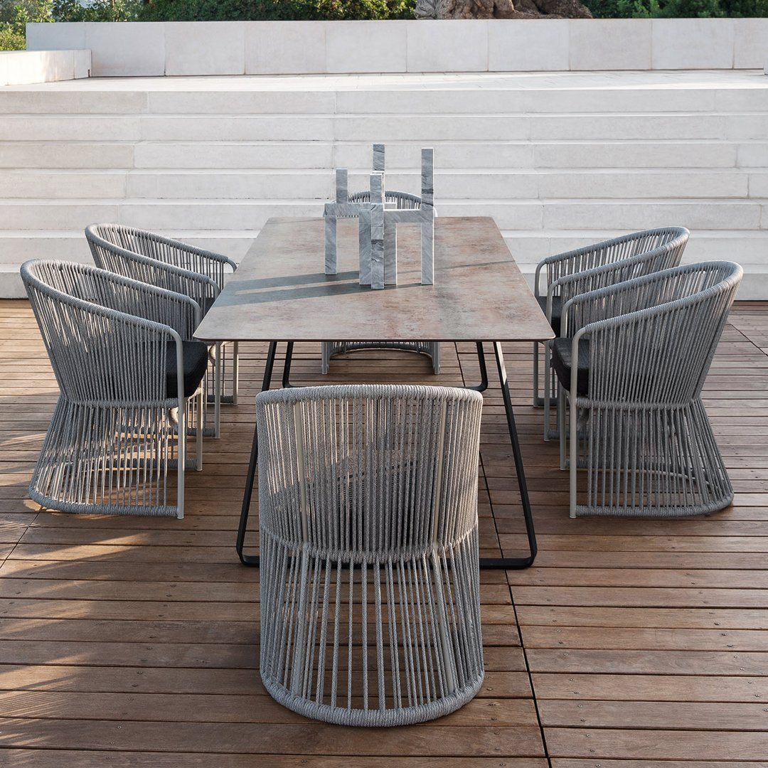 Gray woven chairs surrounding a rustic wooden table, set on a wooden deck. Clean, modern outdoor dining aesthetic.