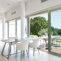 Modern white dining area with sleek glass doors and natural green scenery outside, promoting a bright, airy feel.