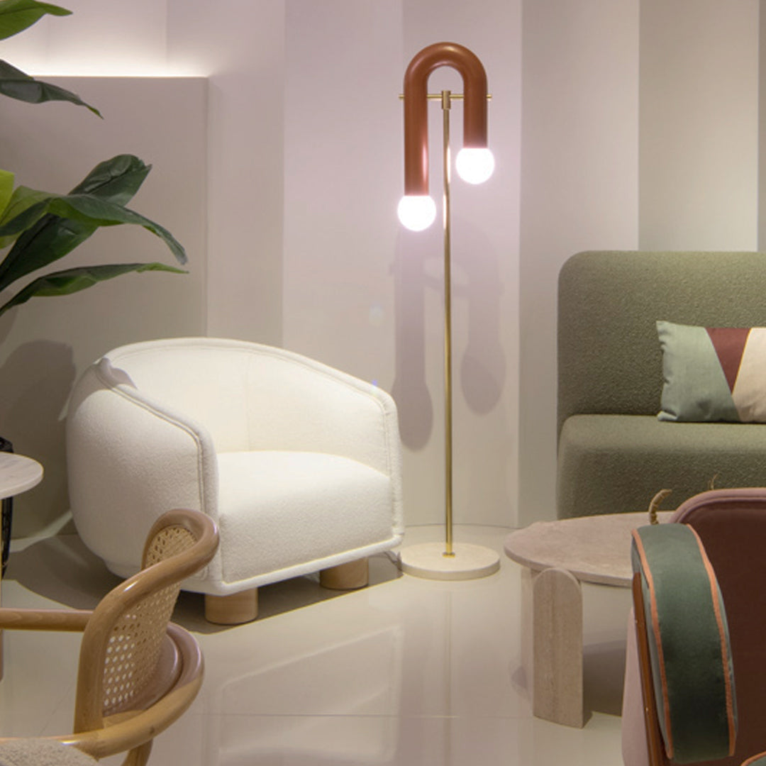 White textured armchair, geometric green and burgundy cushions, copper lamp with round bulbs, and neutral-toned decor elements.