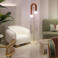White textured armchair, geometric green and burgundy cushions, copper lamp with round bulbs, and neutral-toned decor elements.