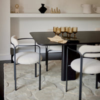 Elegant black table with white upholstered chairs, textured light rug, and warm gold accents. Modern minimalist dining setup.
