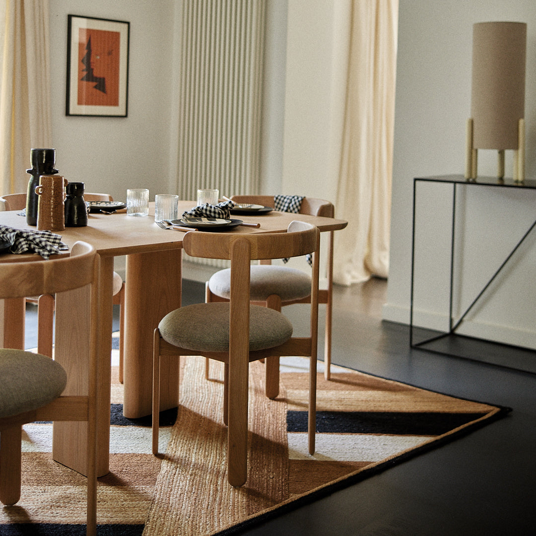 Modern dining room with a geometric rug featuring earthy tones, black, and cream patterns amidst natural wood furniture.