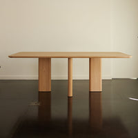 Light wood dining table with a smooth, minimalist design and natural finish, featuring three cylindrical legs.