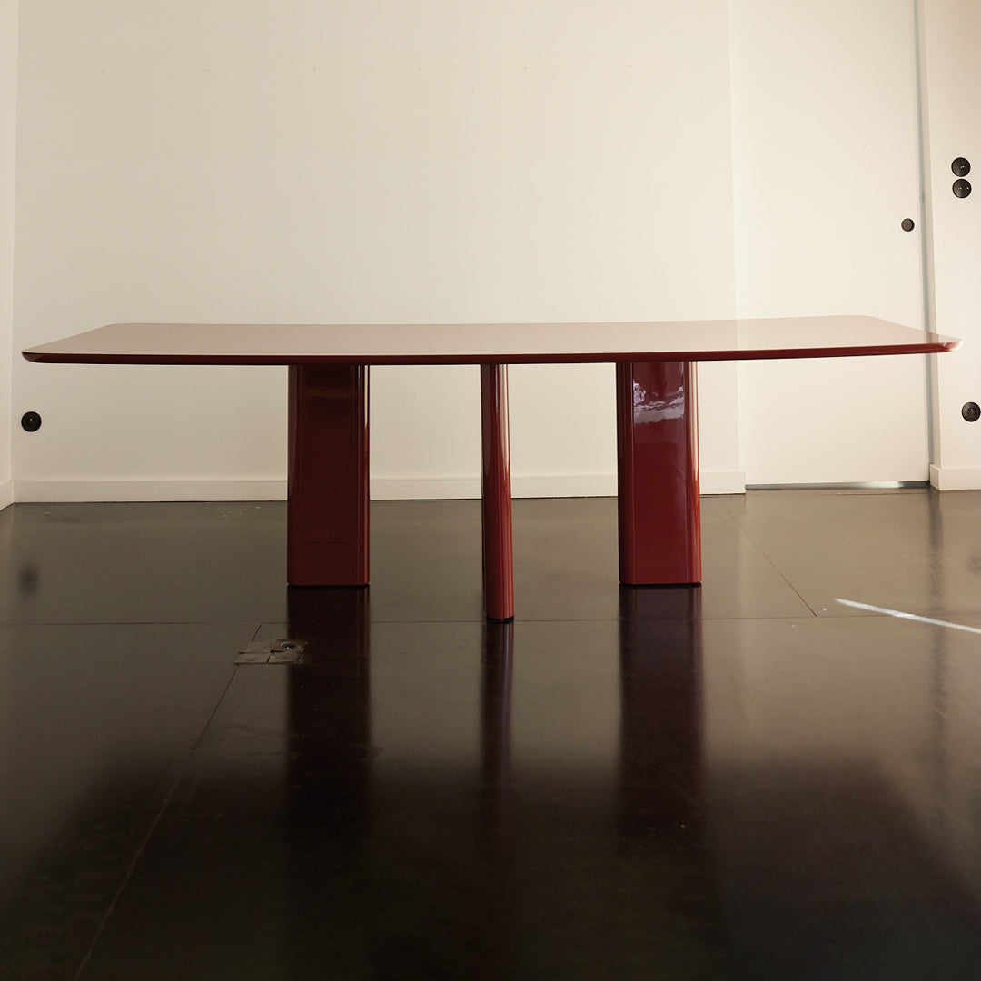 Modern red dining table with a glossy finish and sleek, minimalist design on a dark polished floor.