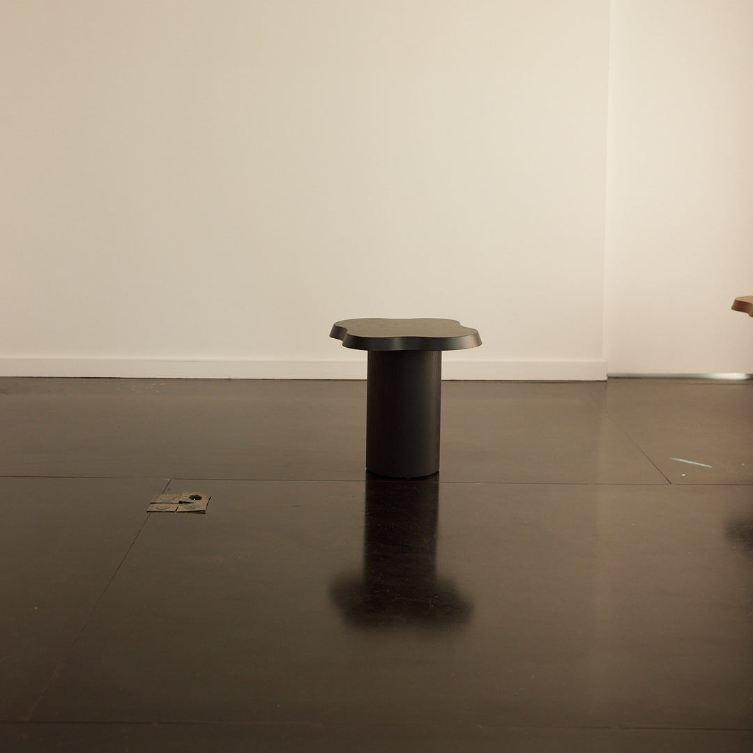 Modern black stool with a sleek cylindrical design and smooth surface, set against a minimalist white backdrop.