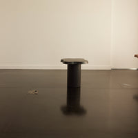 Modern black stool with a sleek cylindrical design and smooth surface, set against a minimalist white backdrop.