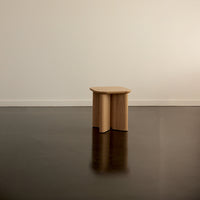 Natural wood stool with a smooth finish and rounded edges, set against a dark floor and minimalistic backdrop.