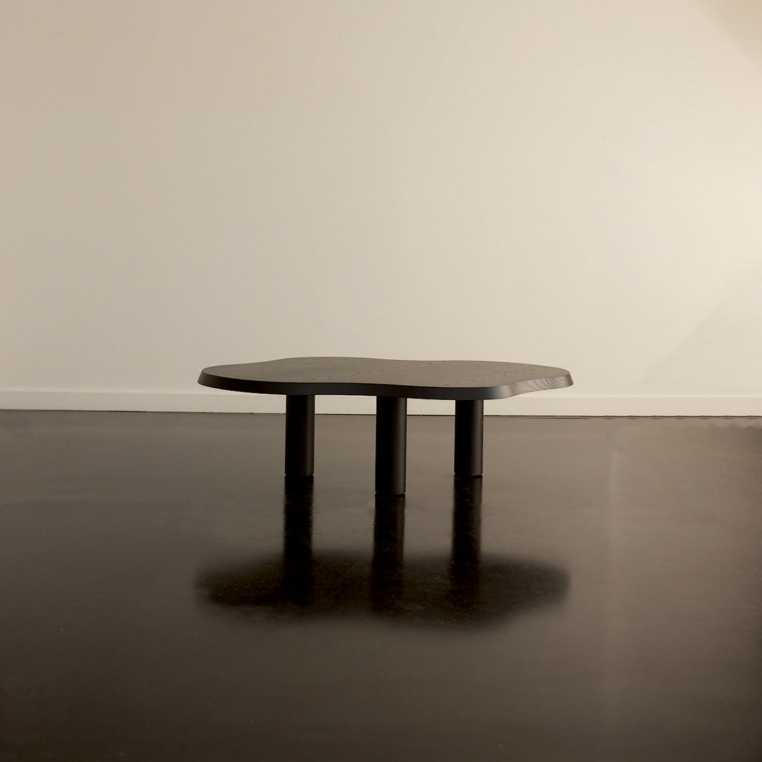 Black modern coffee table with a unique organic shape and three sturdy black legs on a dark floor.