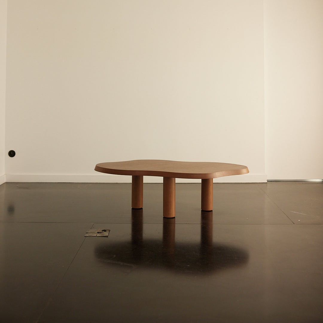 Natural wood coffee table with a smooth, organic shape and three cylindrical legs, set against a minimalistic backdrop.