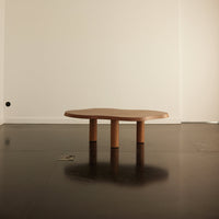 Natural wood coffee table with a smooth, organic shape and three cylindrical legs, set against a minimalistic backdrop.