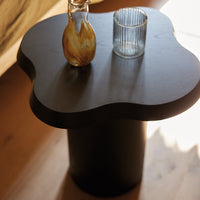 Black organic-shaped table with a smooth surface, featuring a minimalist design and subtle light reflections.