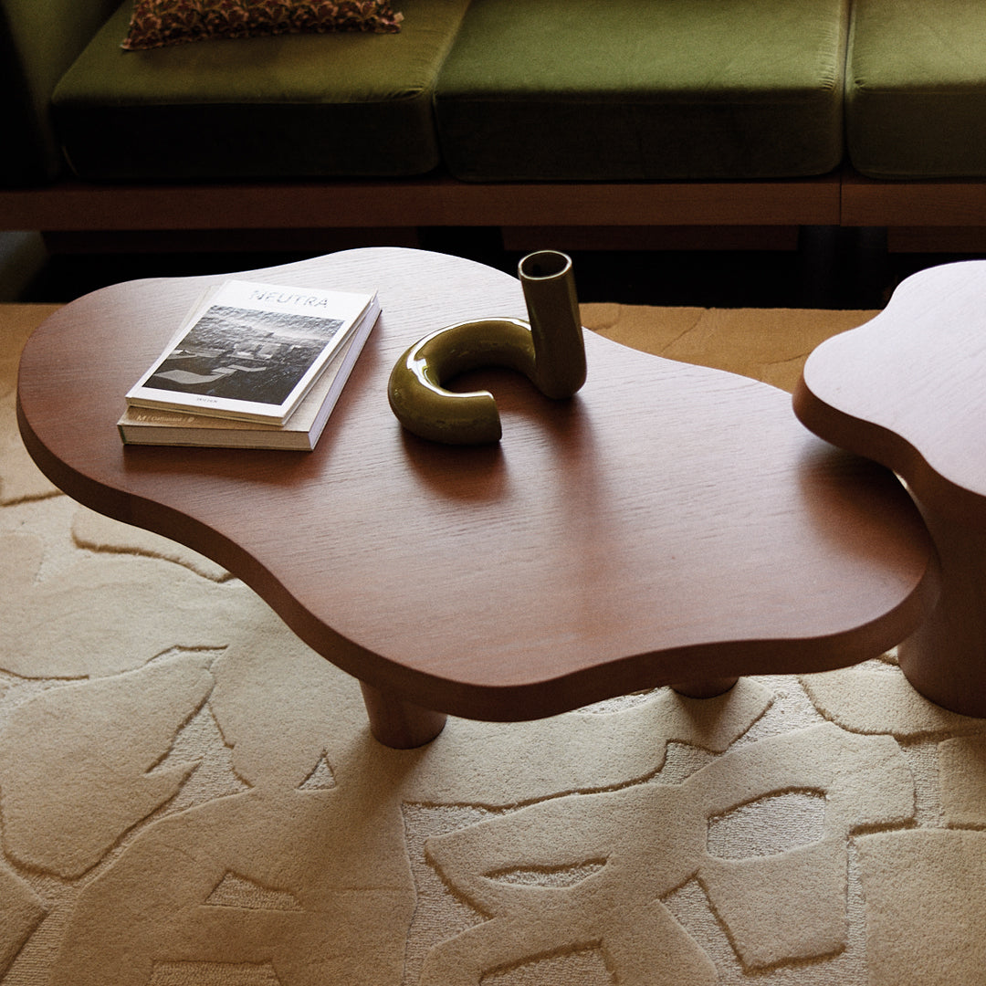"Wooden coffee table with organic shape, rich brown finish, and paired with a textured beige rug."