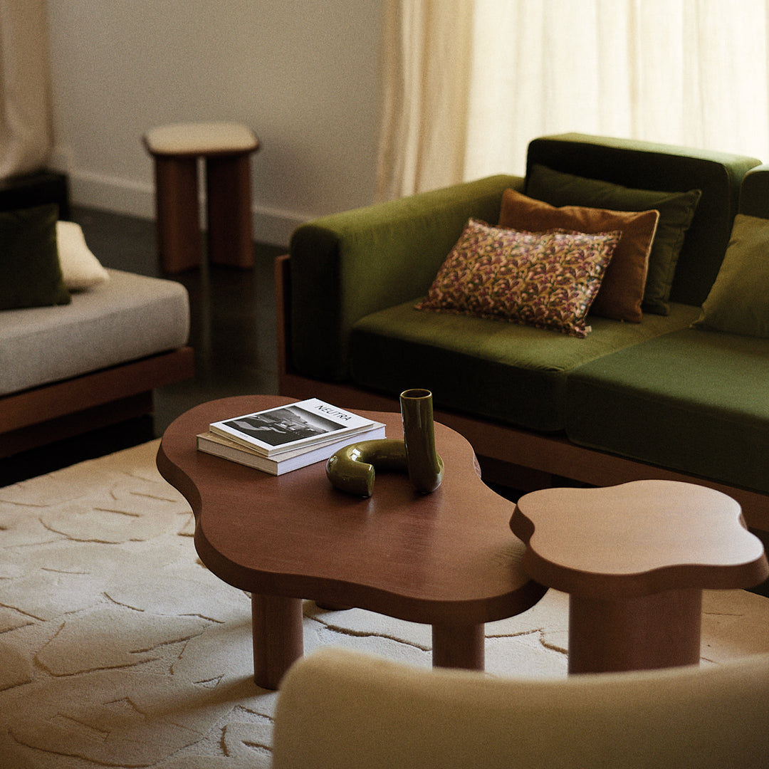 "Modern living room with green and beige sofas, patterned cushions, and a unique wood coffee table against a soft backdrop."