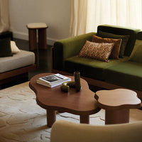 "Modern living room with green and beige sofas, patterned cushions, and a unique wood coffee table against a soft backdrop."