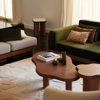 Modern living room with olive green and beige sofas, patterned cushions, and earthy-toned furniture on a textured rug.