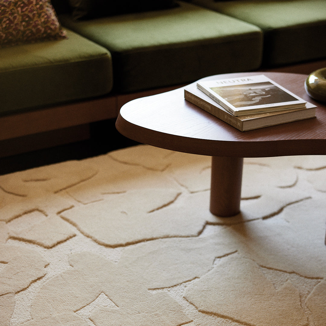 Beige area rug with abstract light and dark beige patterns, paired with a green sofa and wooden coffee table.
