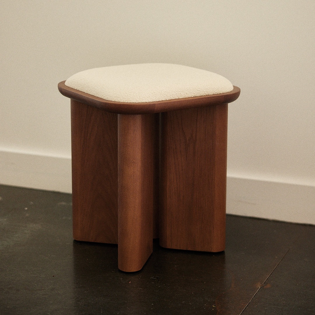 Wooden stool with a rich brown finish and a soft cream cushion top, featuring curved edges and a minimalistic design.