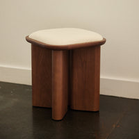 Wooden stool with a rich brown finish and a soft cream cushion top, featuring curved edges and a minimalistic design.