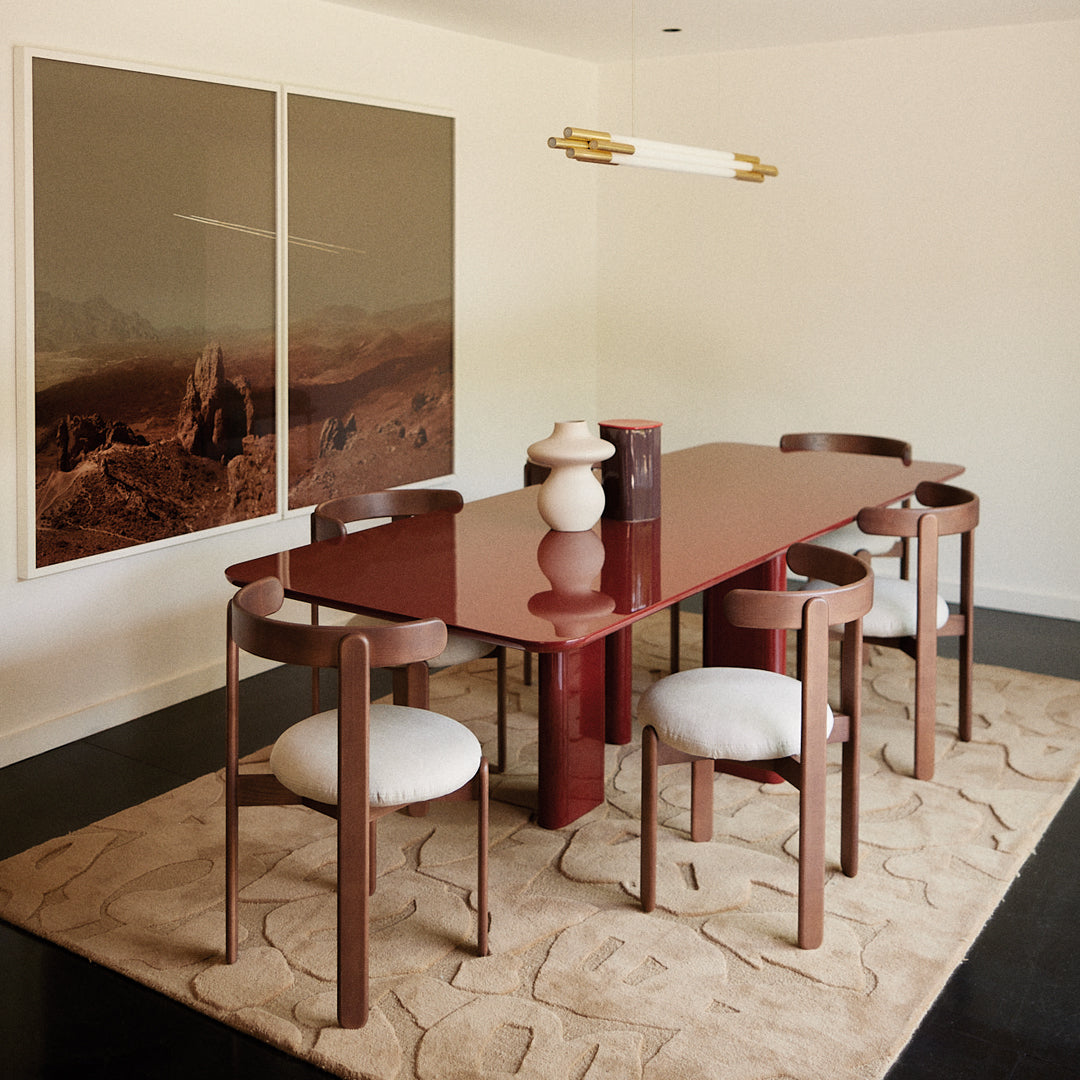 Sleek burgundy dining table with matching chairs, soft white cushions, and a neutral textured rug. Modern minimalist decor.