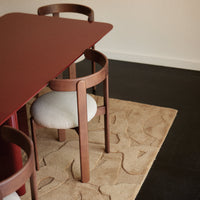 Rust-colored table with rounded wooden chairs on a beige patterned rug, set against a dark floor.