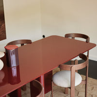Glossy burgundy dining table with wooden chairs featuring circular backs and cream upholstery. Modern minimalist design.