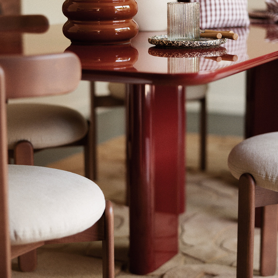 Glossy red dining table with matching brown chair legs, beige upholstery, and subtle textured elements.