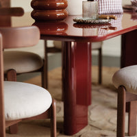 Glossy red dining table with matching brown chair legs, beige upholstery, and subtle textured elements.