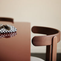 Brown table surface with glossy finish, featuring a striped black and white patterned scarf on top, and curved wooden chair.