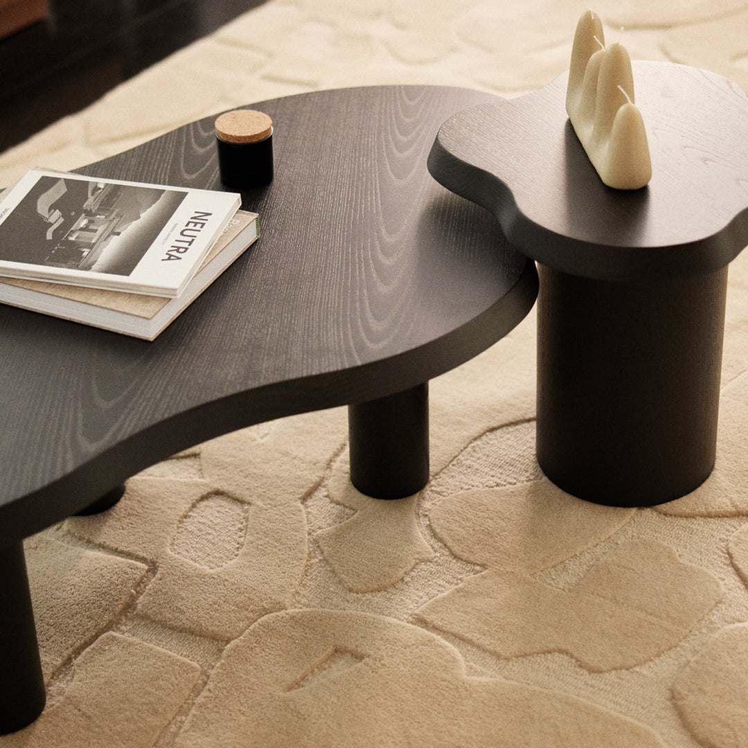 Black, organic-shaped coffee tables with smooth surfaces and contrasting round and cylindrical legs on a textured beige rug.