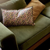 "Colorful patterned pillow with purple, green, and gold florals on a rich olive green couch with a brown accent pillow."