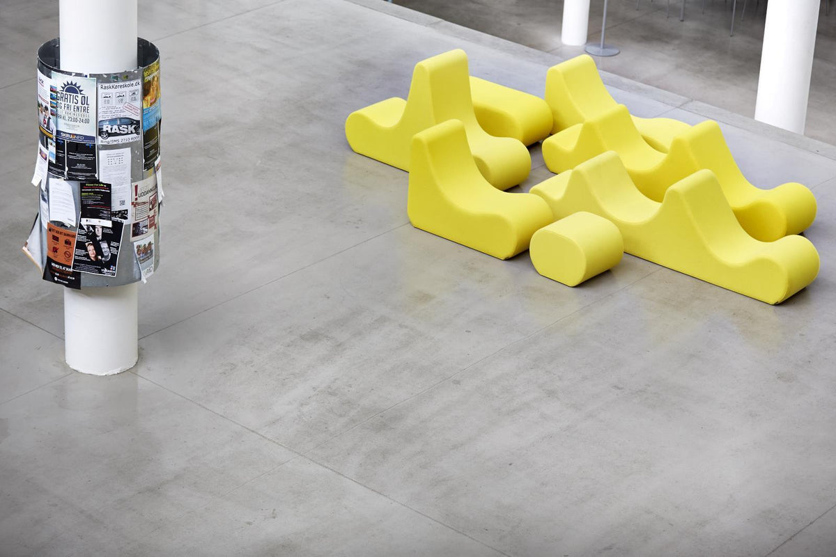 Bright yellow abstract seating arrangement on a gray concrete floor, showcasing playful shapes and a modern aesthetic.