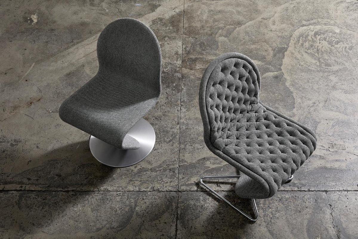 Modern grey upholstered chairs with smooth and tufted textures, set against a rustic concrete backdrop.