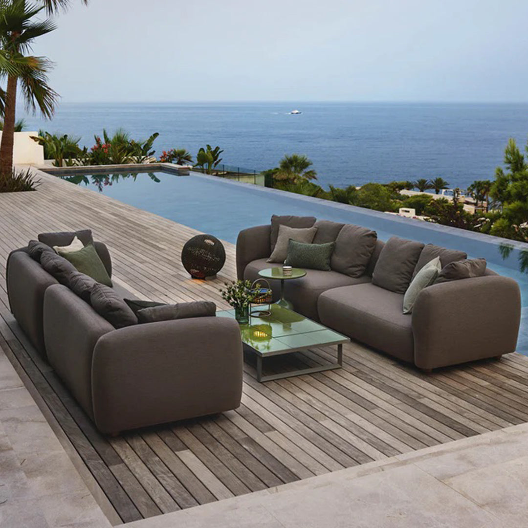 Gray outdoor sectional sofa with plush cushions, set against a serene ocean backdrop and wooden decking.