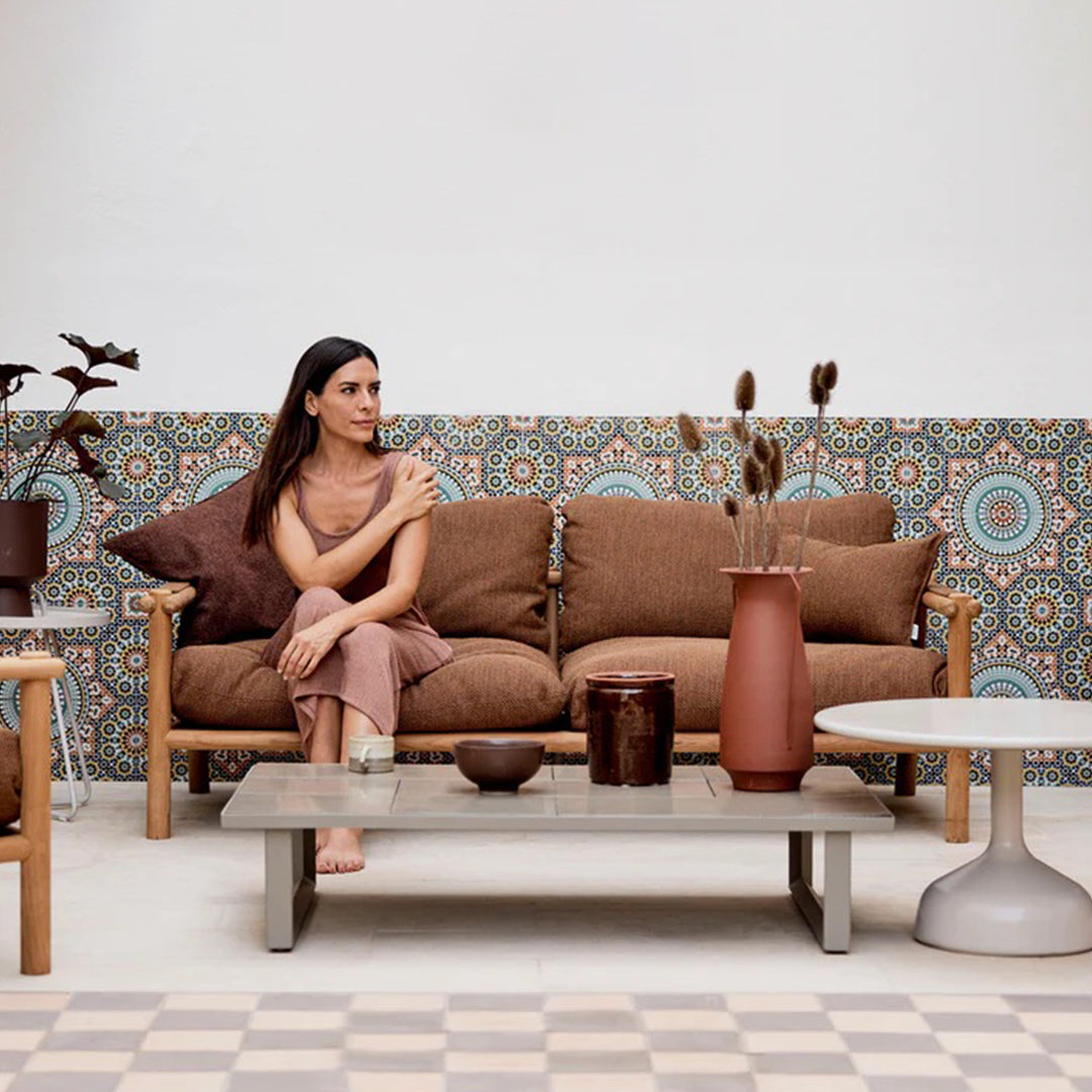 "Brown sofa with patterned backdrop in blue and orange, complemented by earthy-toned decorative vases."