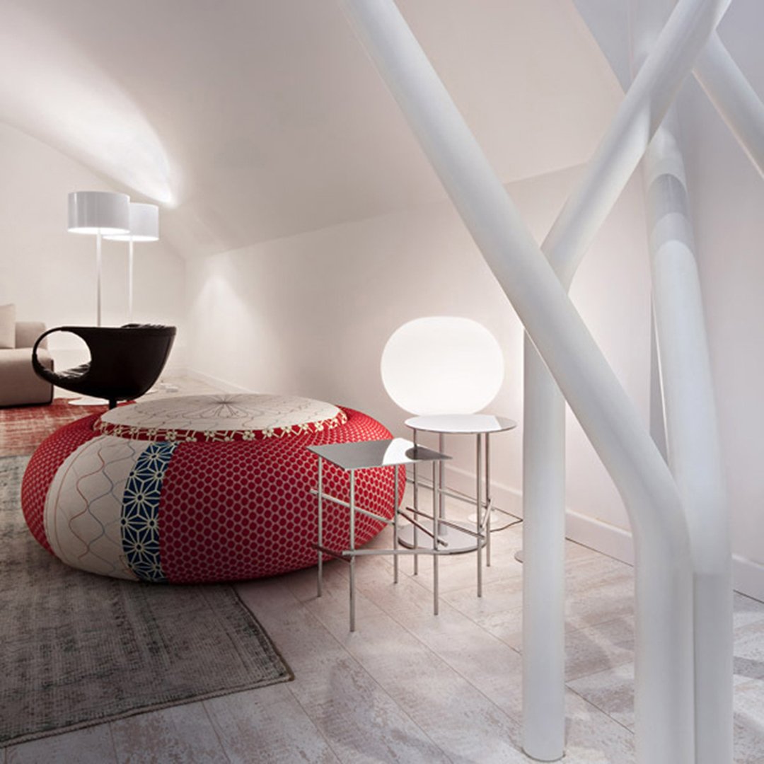 Vibrant red and cream pouf with intricate patterns, contrasted by sleek white lighting and modern furniture elements.