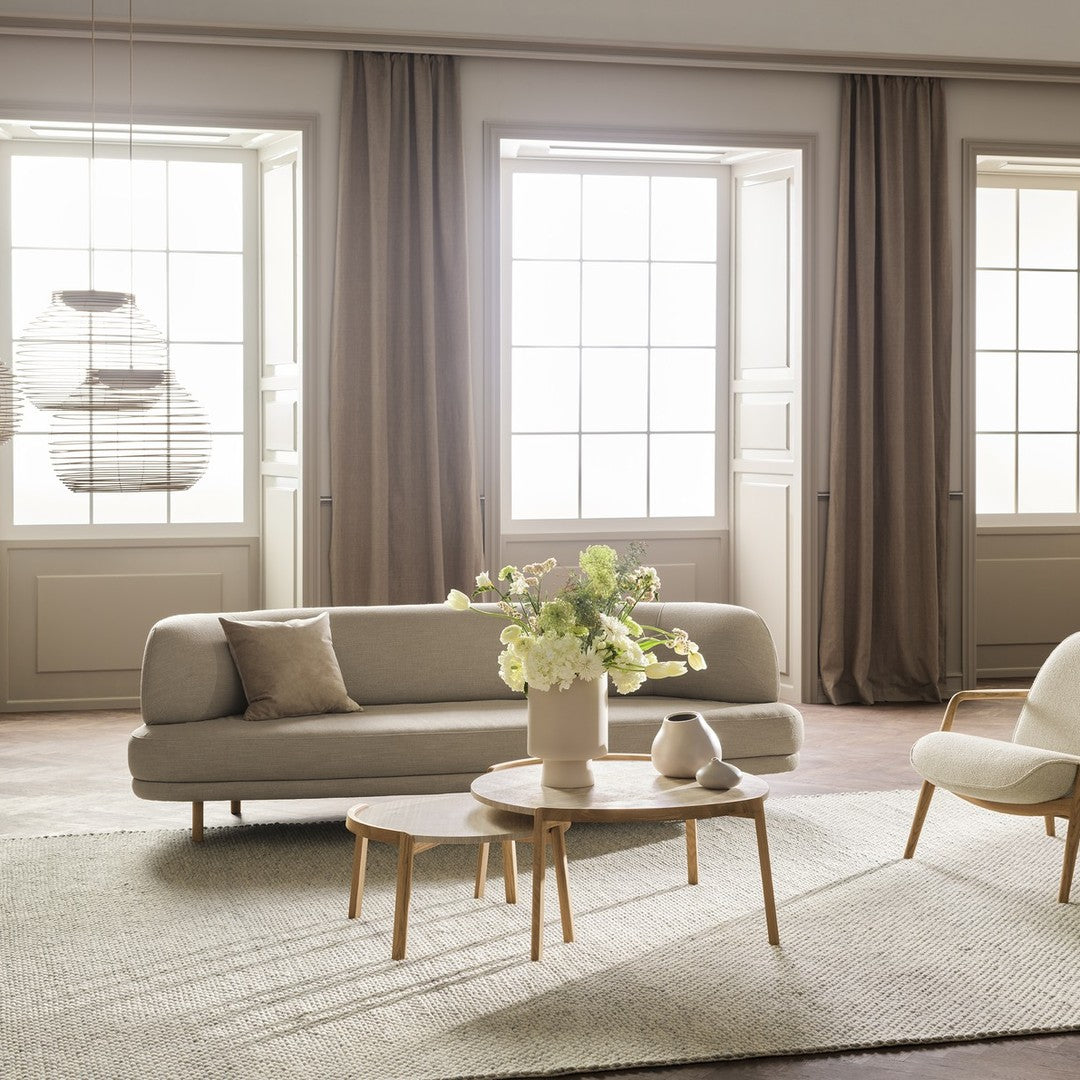 Light gray sofa with beige accents, wooden tables, and soft neutral curtains in a bright, airy room.