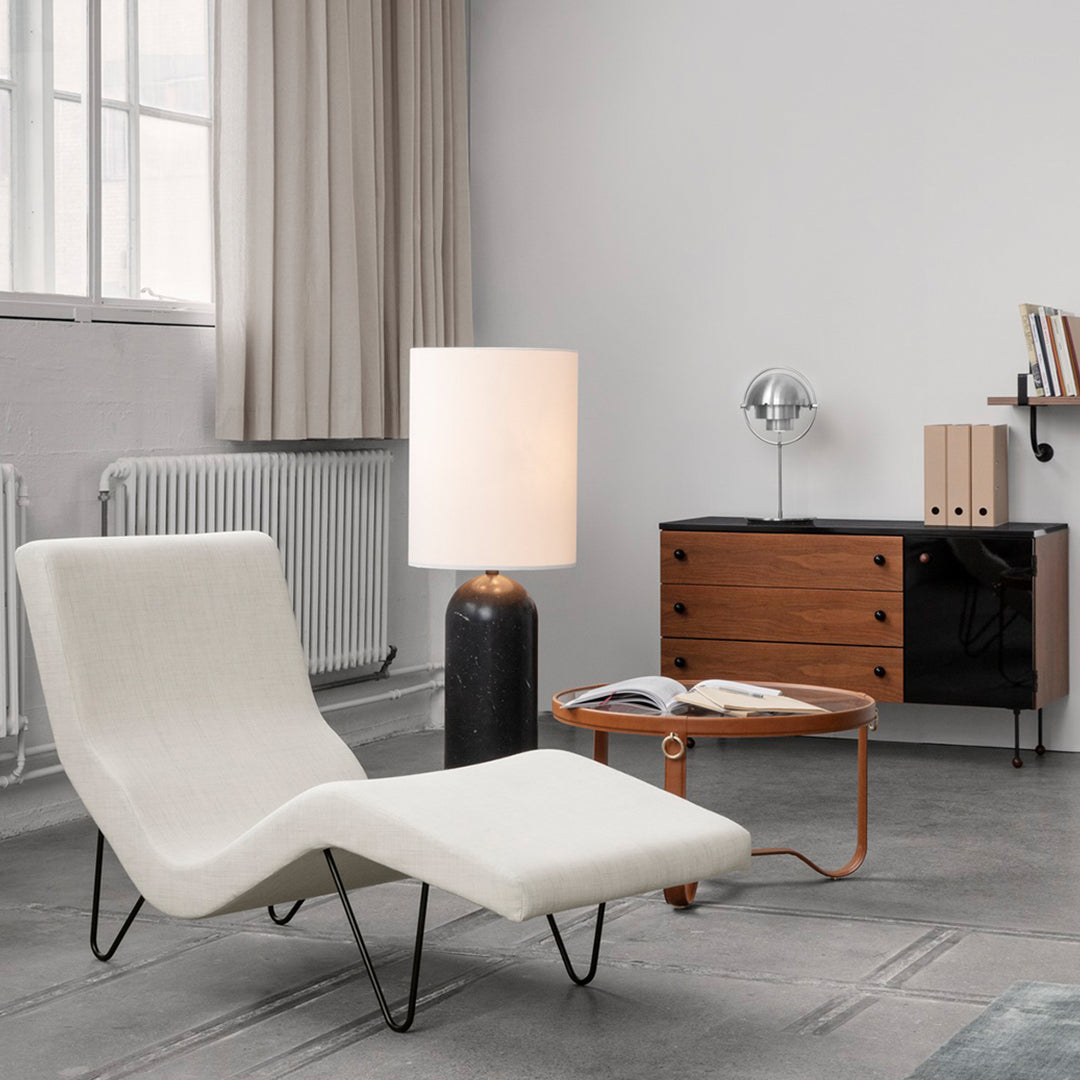 White modern chaise lounge with sleek curves, set against a gray backdrop and complemented by warm wooden accents.