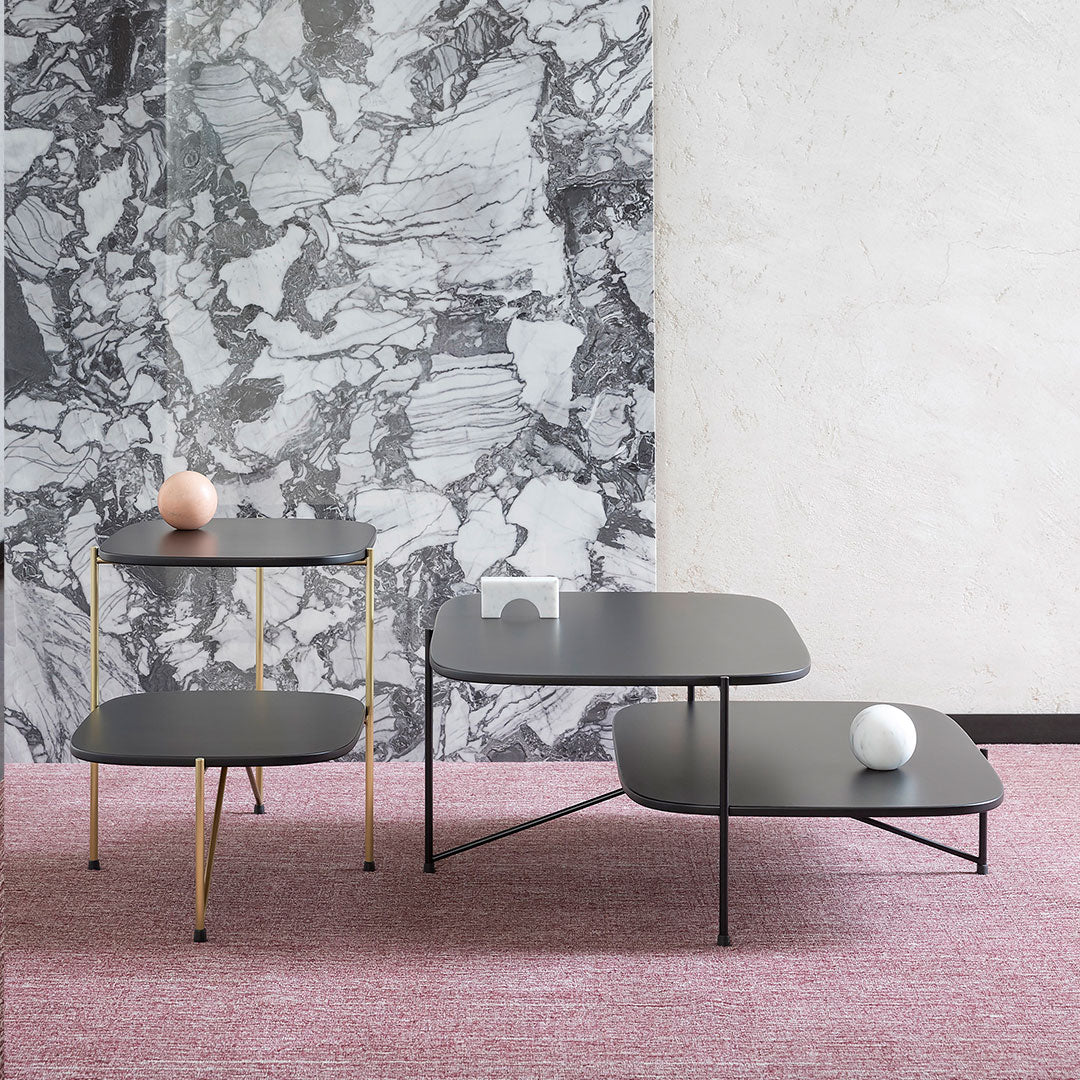Modern black tables with gold and black metal accents, set against a textured gray and pink background.