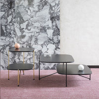 Modern black tables with gold and black metal accents, set against a textured gray and pink background.