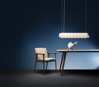 Modern lighting fixture with a cream and transparent design, paired with a beige chair against a dark blue background.