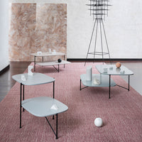 Modern coffee tables with light gray tops on black legs, set on a textured pink rug, against a neutral backdrop.