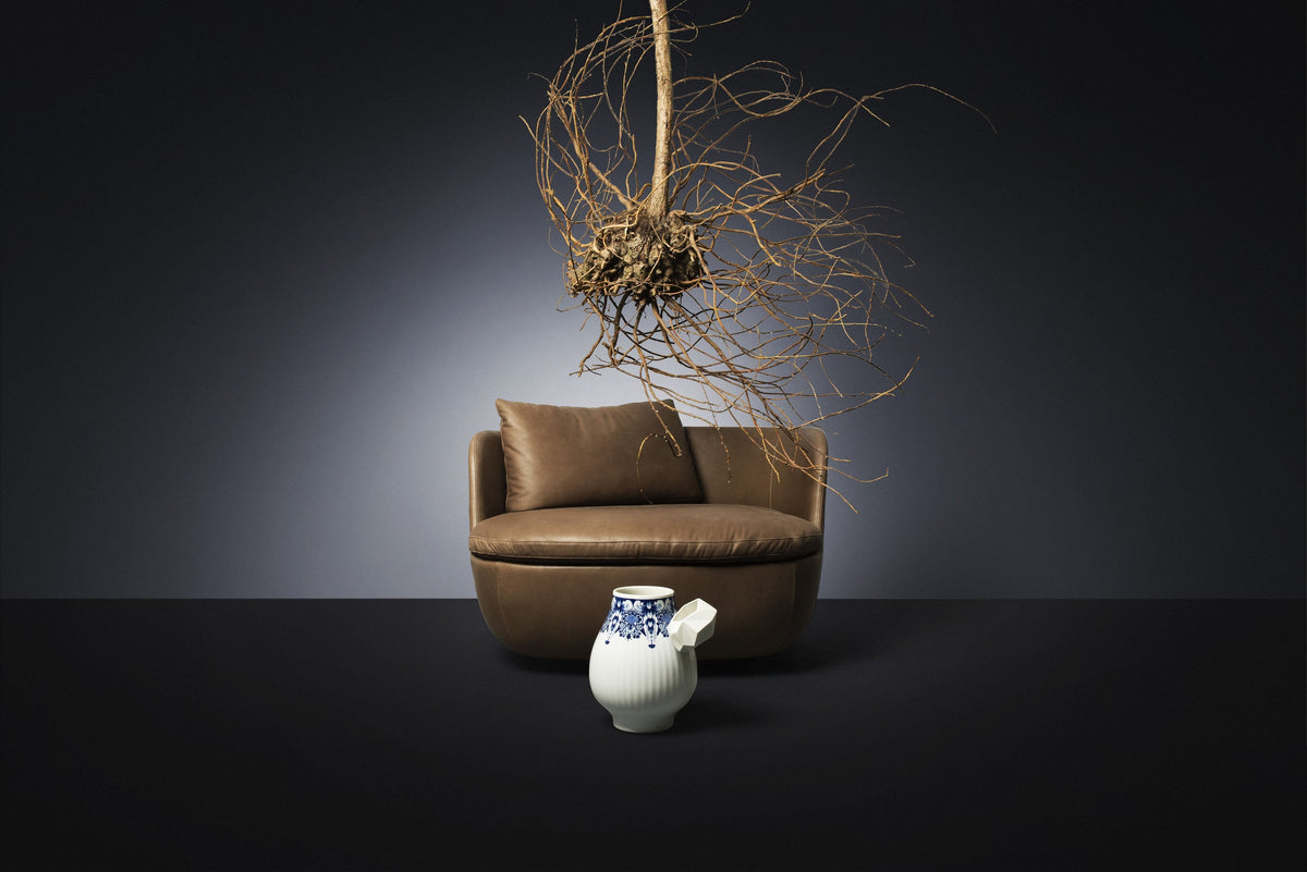 Brown leather curved sofa with a white and blue ceramic jug against a dark background, featuring organic root decor.