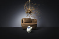Brown leather curved sofa with a white and blue ceramic jug against a dark background, featuring organic root decor.