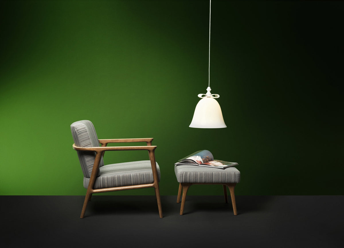 Gray upholstered armchair with light wood accents, cozy ottoman, and a white pendant light against a deep green wall.